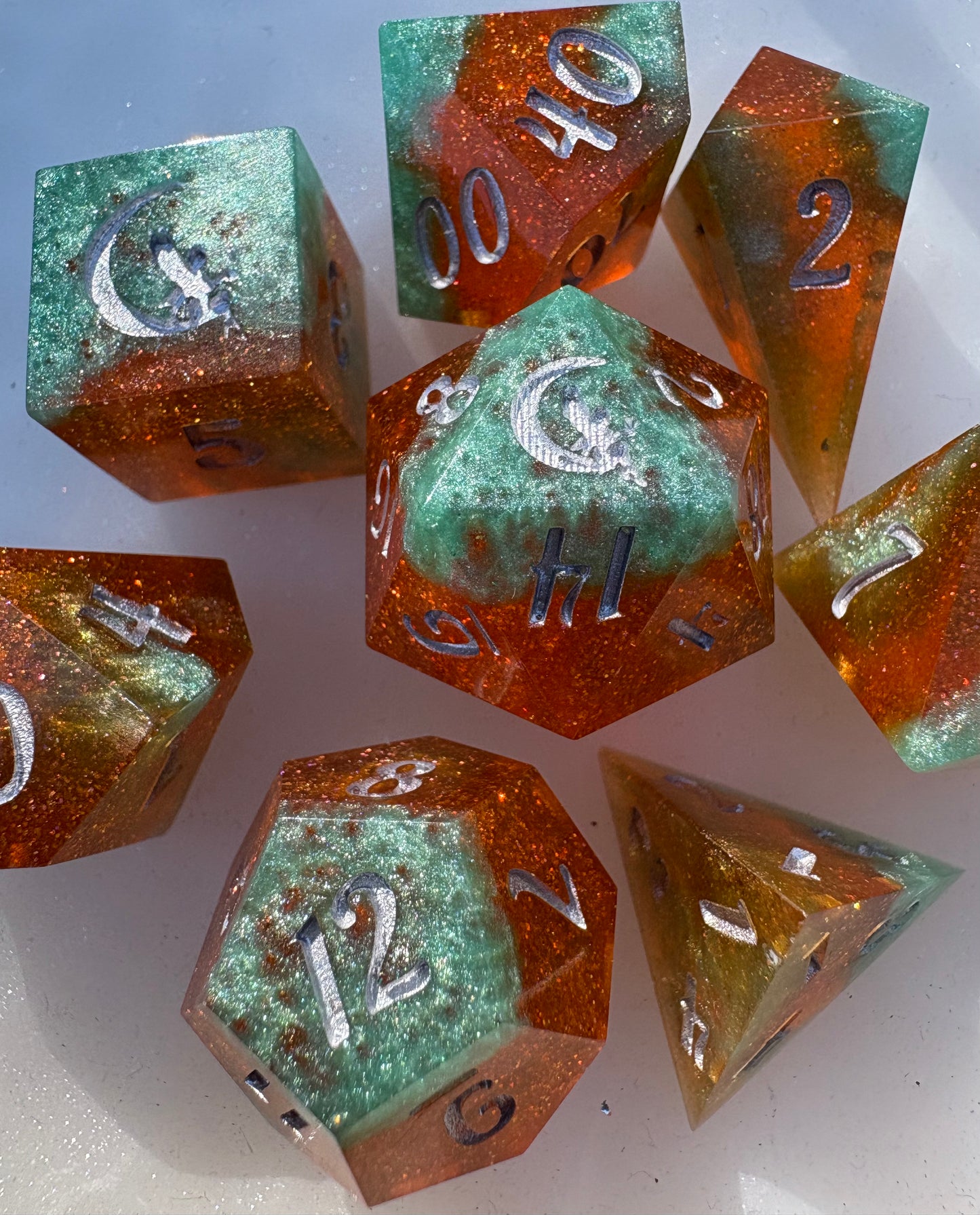 Set of polyhedral dice with green and orange glittery finish on a white background