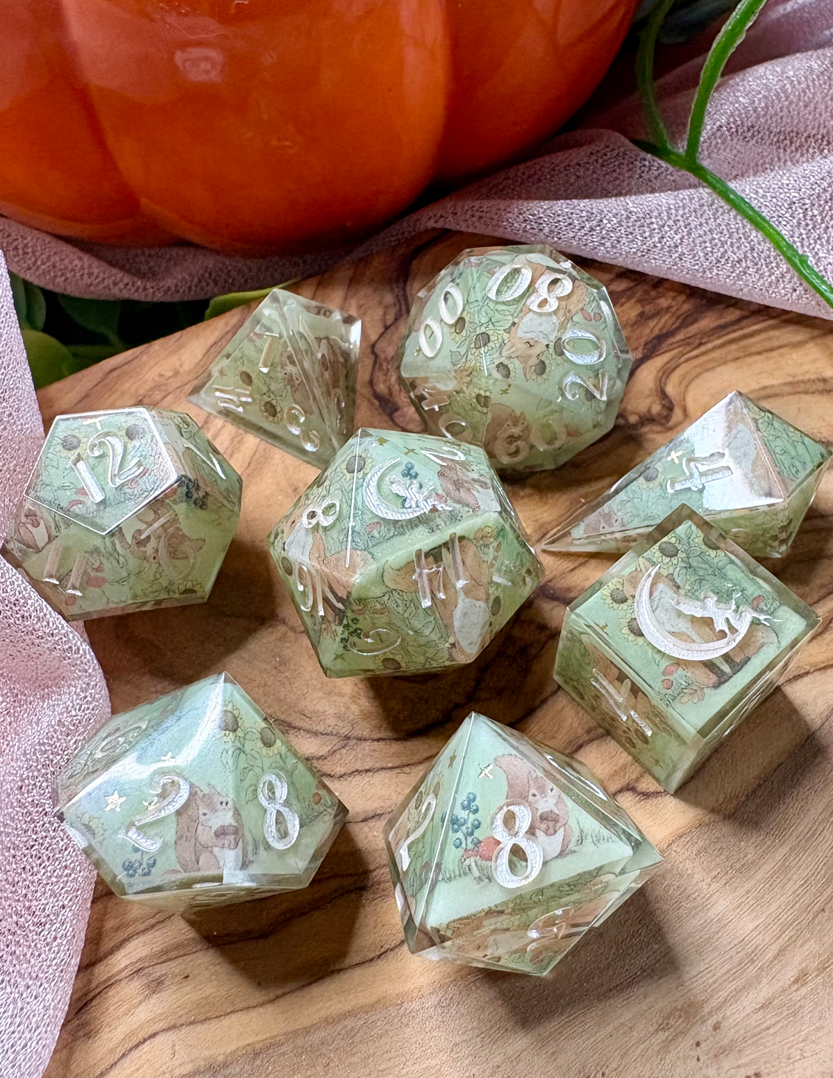 a handmade dice set with a green background and foxes, squirrels, and autumn flora