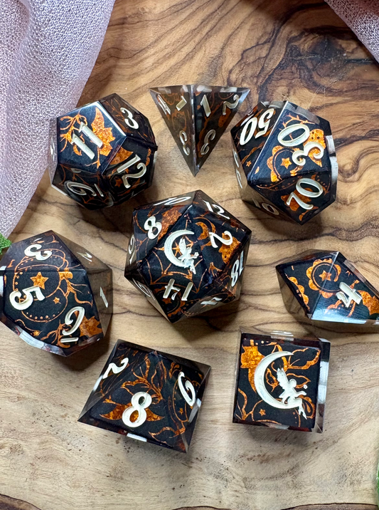 a set of black polyhedral dice with glittery orange Halloween designs