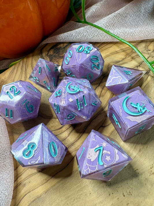 a set of purple polyhedral dice with glittery silver Halloween designs and turquoise ink