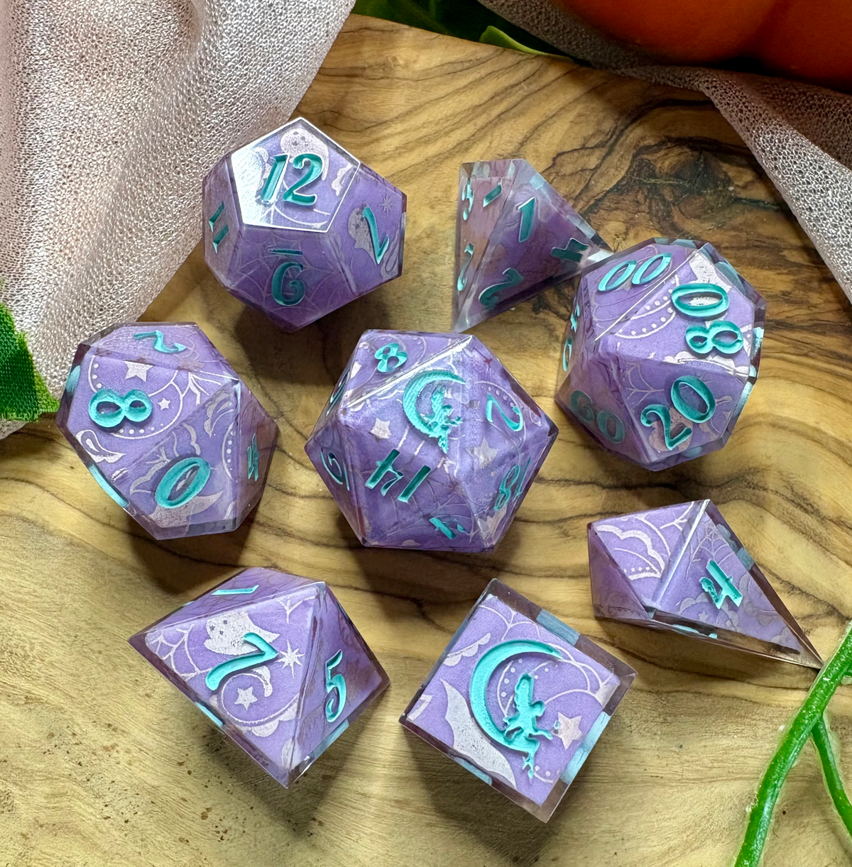 a set of purple polyhedral dice with glittery silver Halloween designs and turquoise ink