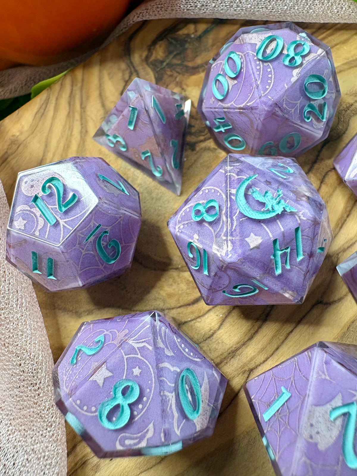a close up view of a set of purple polyhedral dice with glittery silver Halloween designs and turquoise ink